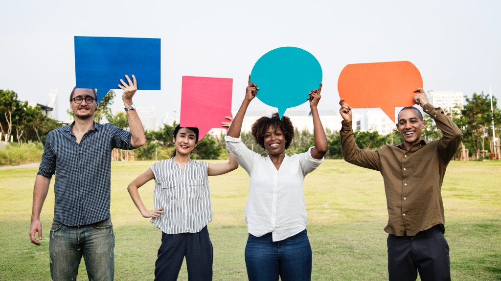 Picture of four people standing outside holding colored pieces of paper in the form of speech bubbles